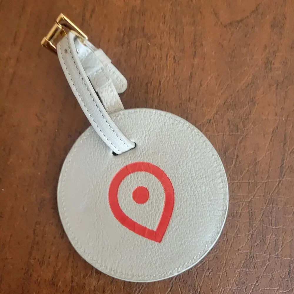 Round textured leather luggage tag in light grey with a red map